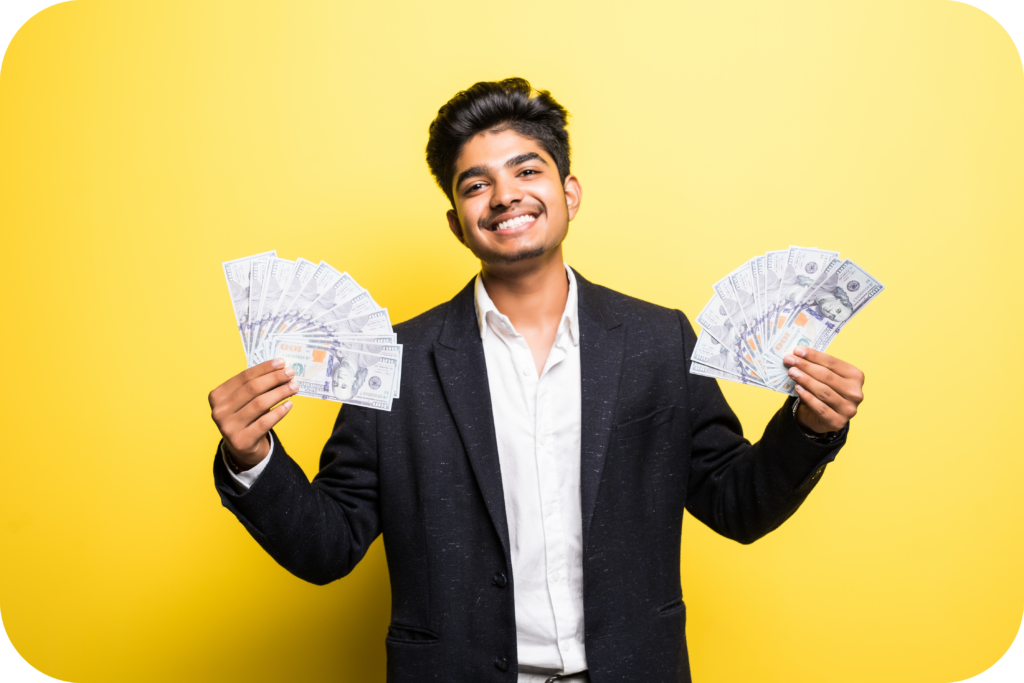 successful-indian-entrepreneur-with-dollar-banknotes-hand-classical-suit-looking-camera-with-toothy-smile-while-standing-against-yellow-wall-modified